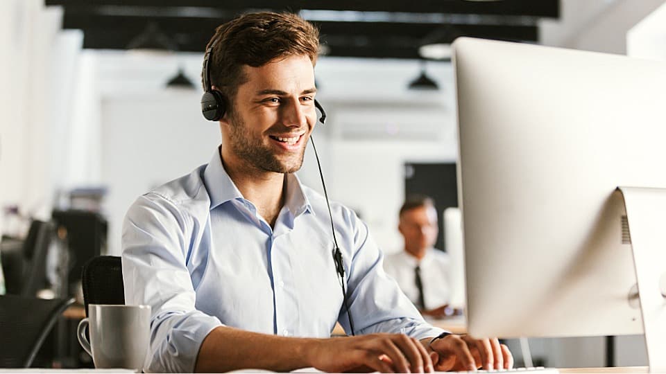 A friendly DACHSER & KOLB project manager wearing a headset advises HR clients at a computer about the current status of an employee assignment.