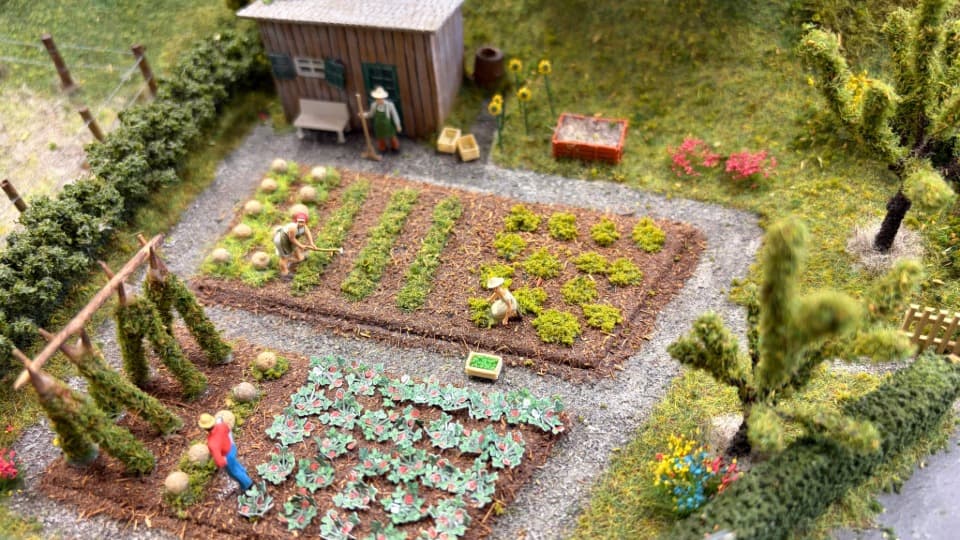Detaillierte Modelleisenbahnanlage mit Miniatur-Figuren im Garten, deren lose Kleinteile vor dem Transport mit DACHSER & KOLB abgenommen werden müssen.