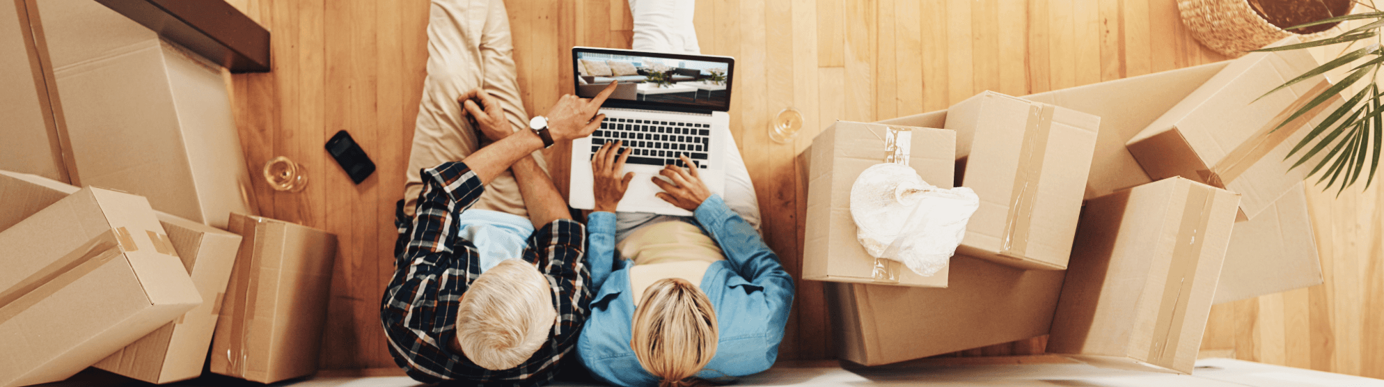 Senior couple calculating moving costs on a laptop, surrounded by cardboard boxes in their new home