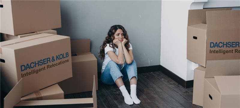 Junge Frau sitzt traurig zwischen Umzugskartons – Symbolbild für emotionale Belastung durch Umzugsdepression.