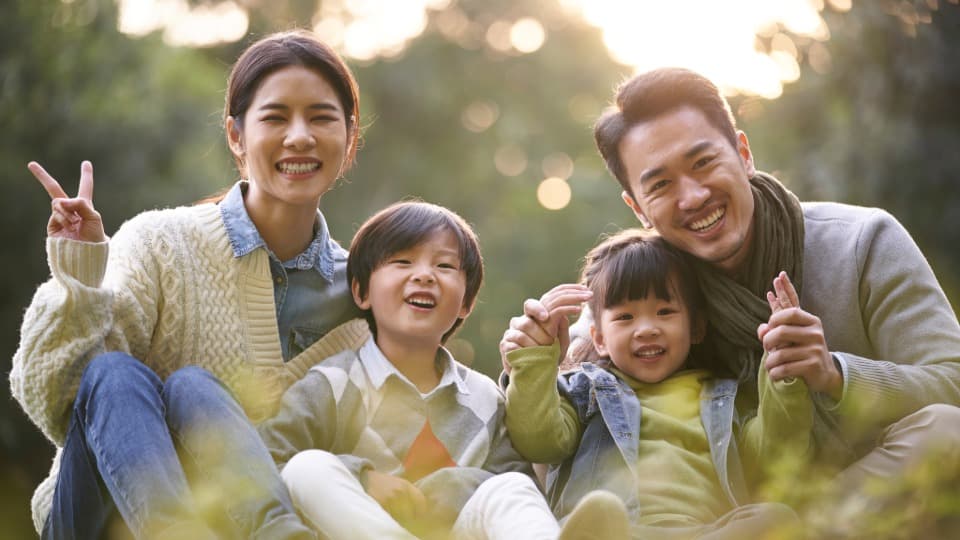 Eine taiwanische Familie sitzt auf einer Wiese und lächelt in die Kamera