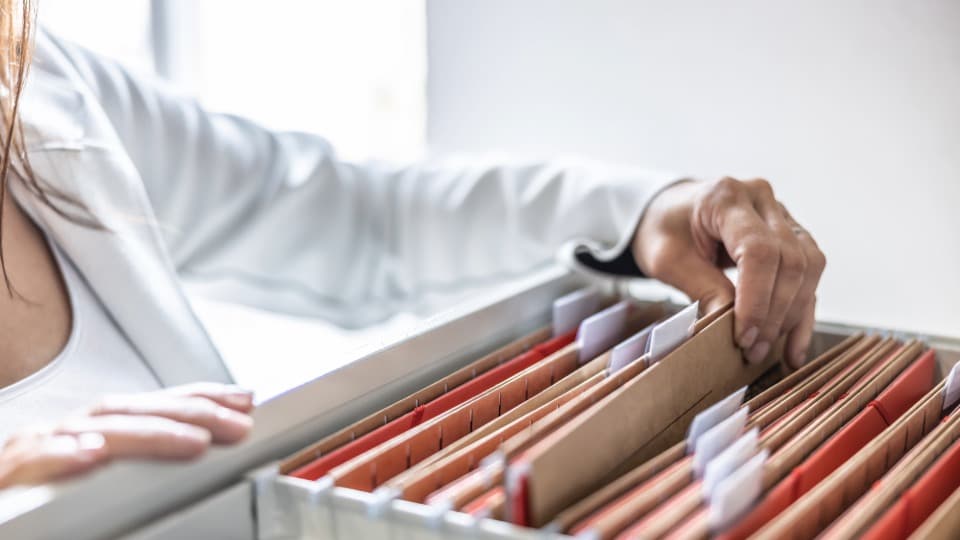 Data security during a public authority relocation – An employee sorts confidential documents into hanging file folders in an archive drawer.