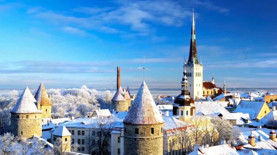 Verschneite Altstadt von Tallinn mit Kirchturm und historischen Türmen unter blauem Winterhimmel