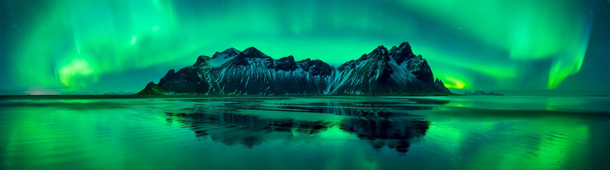 Nordlichter über schneebedeckten Bergen und spiegelndem Wasser in Island