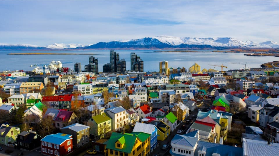 Stadtansicht von Reykjavík mit bunten Häusern, Küste und schneebedeckten Bergen im Hintergrund
