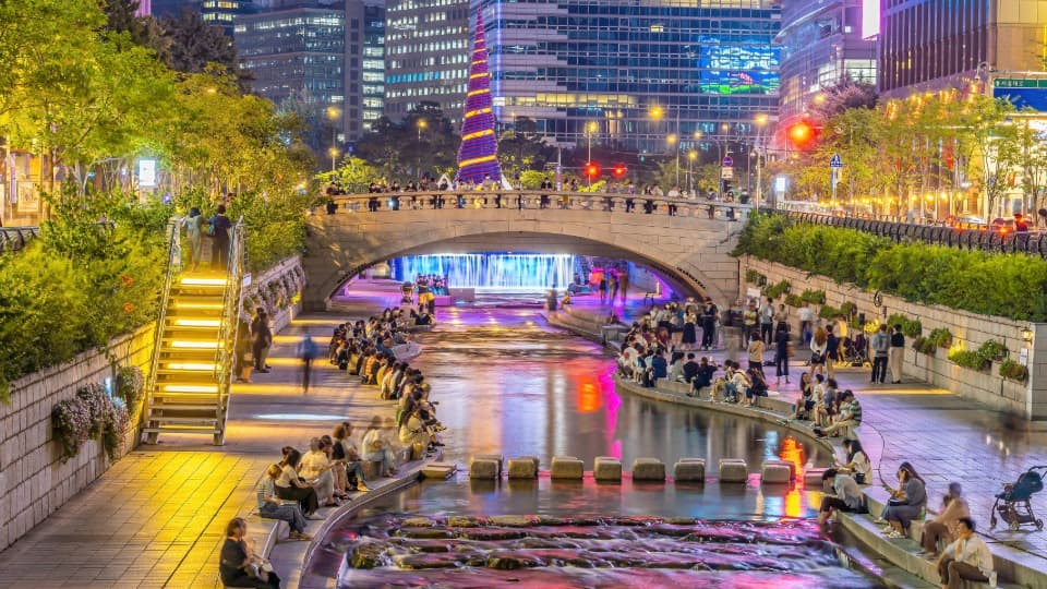 Busy Cheonggyecheon stream in Seoul at night with bridge, lights and pedestrians