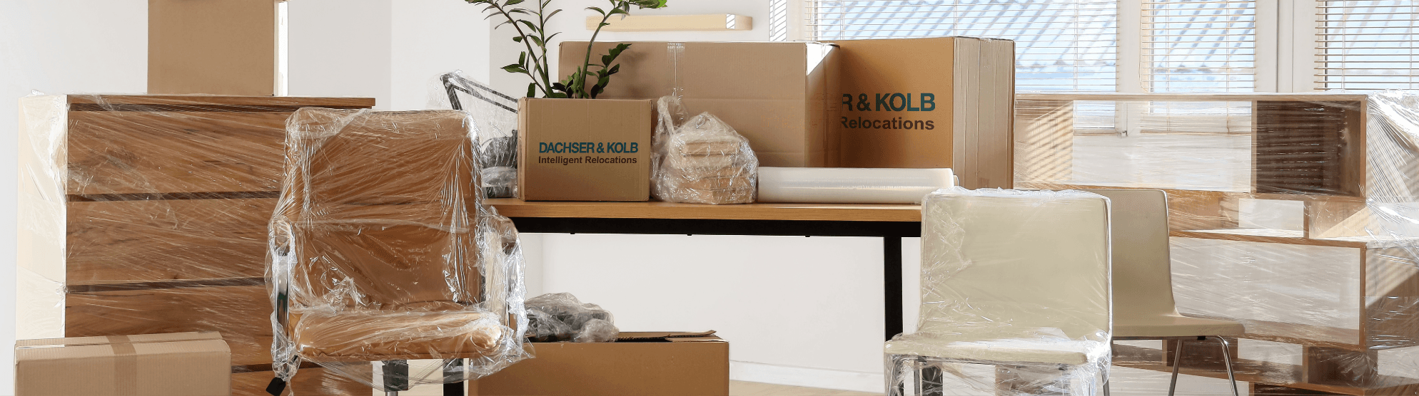Wrapped office furniture and moving boxes with DACHSER & KOLB emballage in a bright office before relocation
