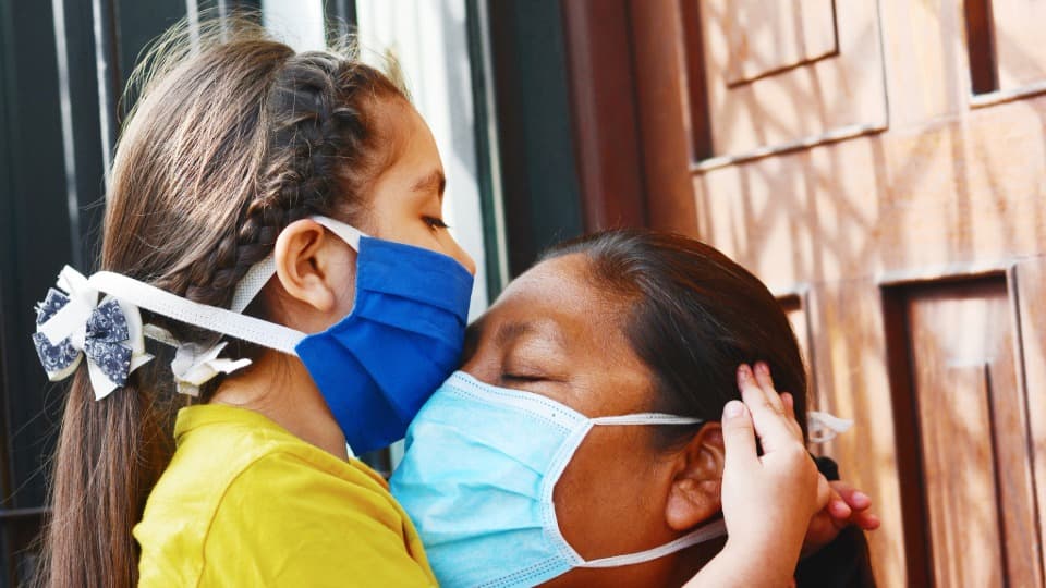 Gesundheit in Peru: Ein Mädchen mit Maske umarmt eine ebenfalls maskierte Person