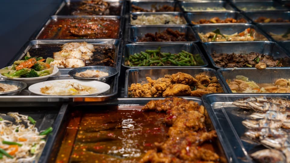 Hawker Culture in Singapur: Verschiedene Speisen sind in einem Buffet in einem Gemeinschaftsraum aneinandergereiht