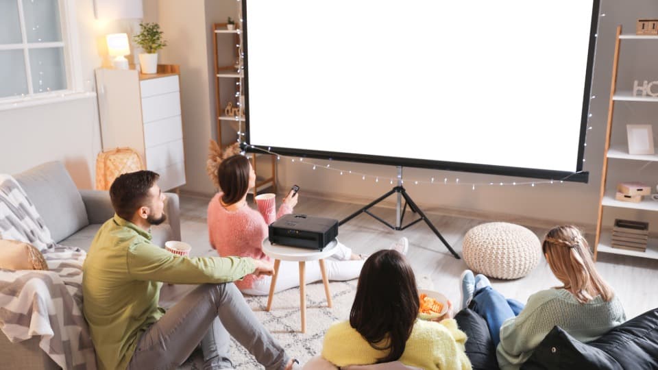 Eine Gruppe von Freunden im Heimkino vor einer großen Beamer-Leinwand mit einem Projektor vor dem sicheren Transport durch DACHSER & KOLB.