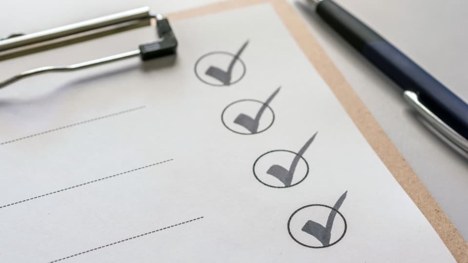 A structured checklist with completed tick boxes on a clipboard beside a pen – symbol image for transparent project execution by DACHSER & KOLB.