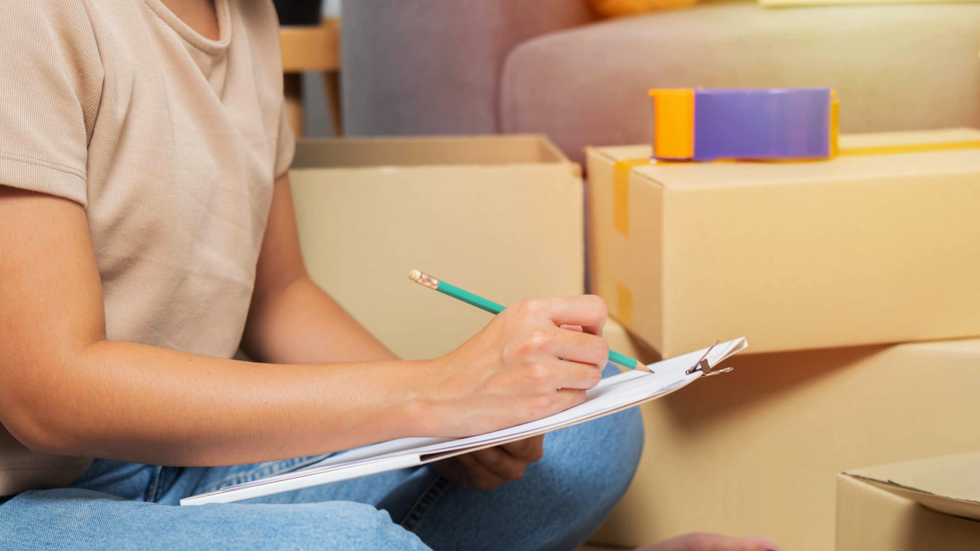 Person sitzt inmitten von Umzugskartons und erstellt eine Inventarliste, typisch für einen "Packed by Owner" (PBO) Umzug.
