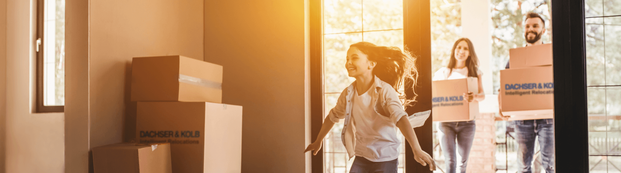 Happy family during private move – child runs joyfully into new home while parents carry moving boxes inside..