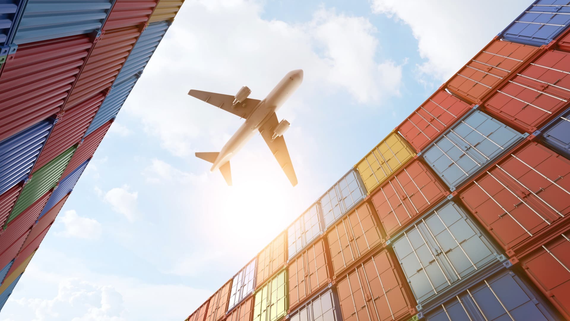 Flugzeug über gestapelten bunten Containern – Symbol für Terminal Handling Charges im globalen Handel.