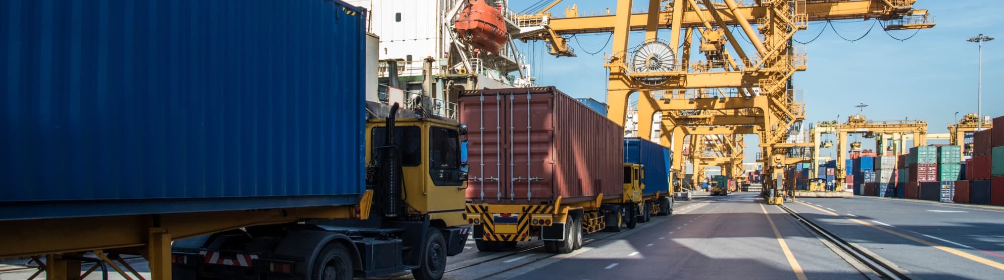 LKW mit Containern im Containerterminal, Hafenkräne im Hintergrund – TEU-basierte Containerlogistik