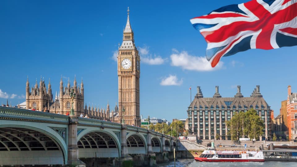 Big Ben and Westminster Bridge in London with a UK flag under a blue sky