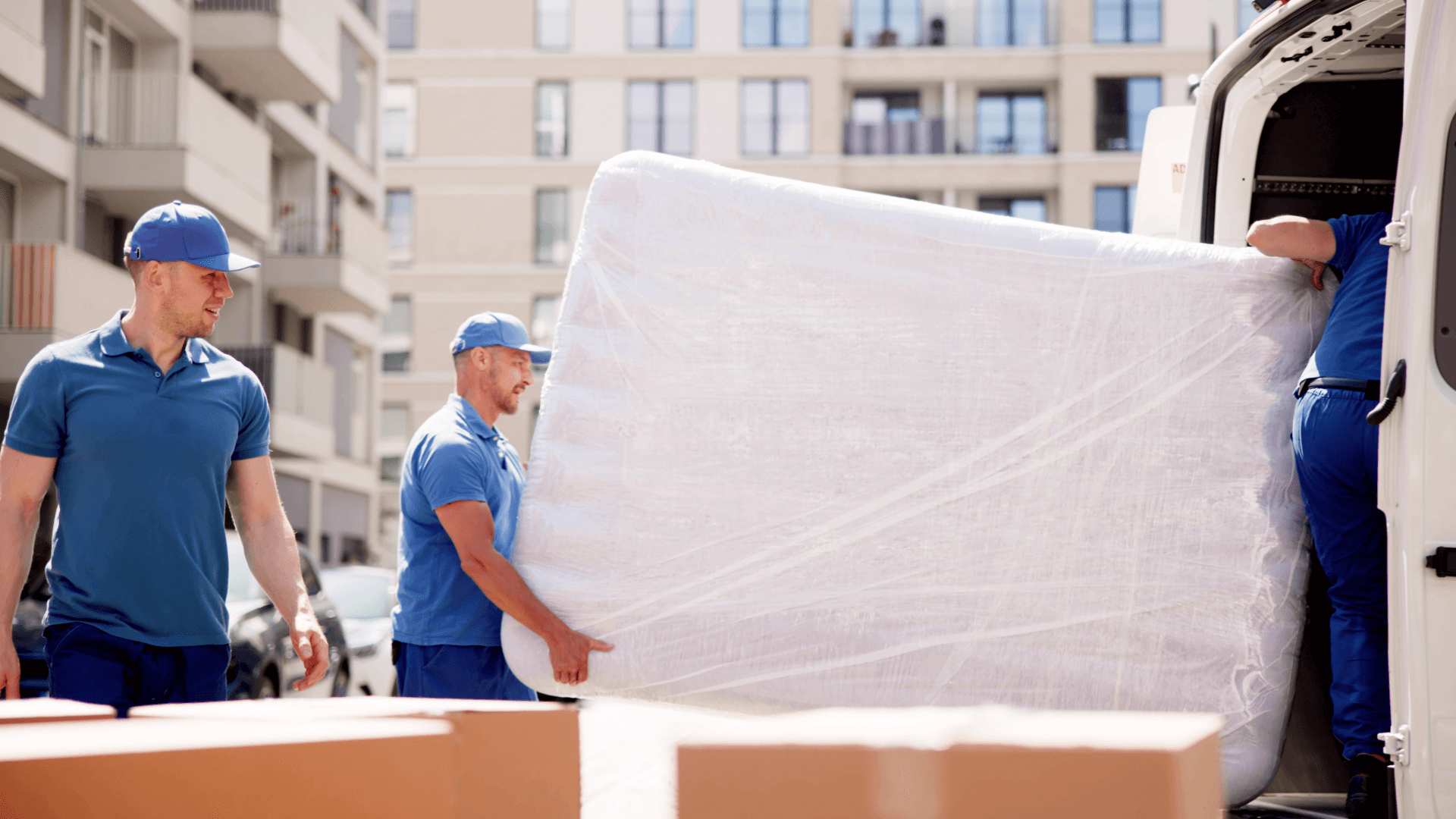 Moving Berlin Stuttgart: Movers carrying mattress into moving van. Accessible image.