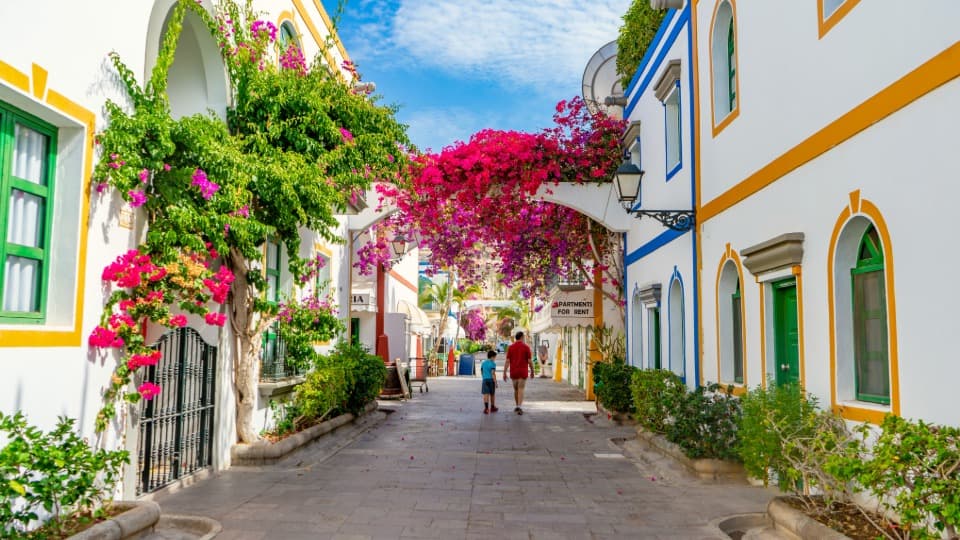 An idyllic alley with white houses and blooming bougainvillea in Puerto de Mogán, Gran Canaria, representing moving box transport services by DACHSER & KOLB.