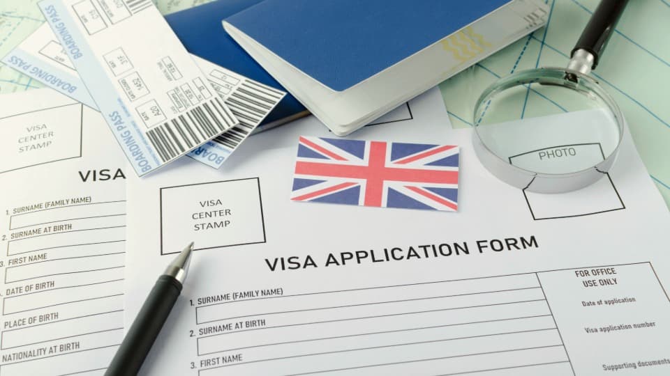 UK visa application forms with passport, boarding passes and magnifying glass on a desk