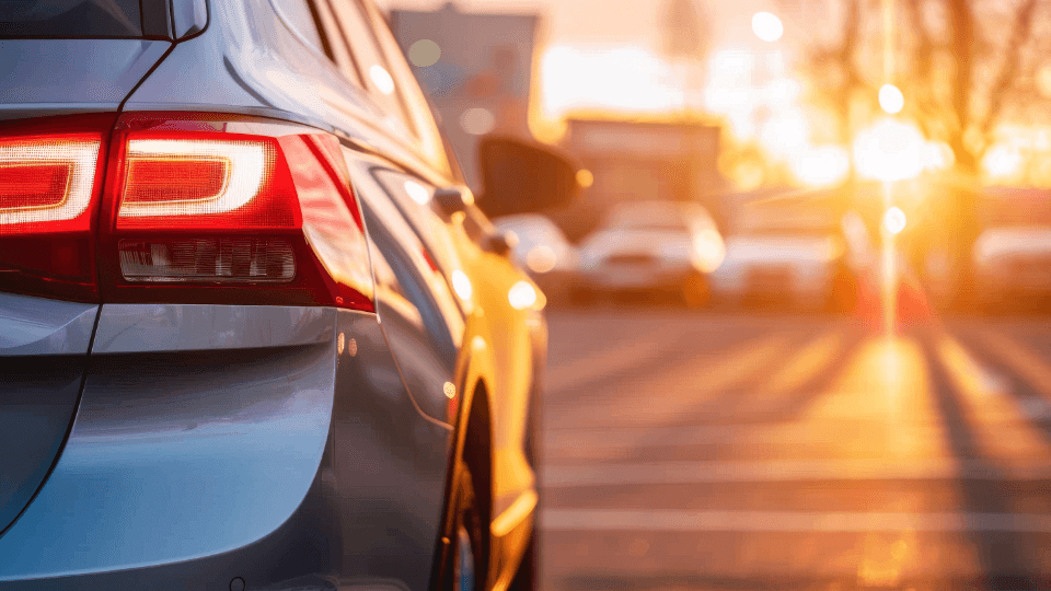 Rear view of a silver car in a parking lot at sunset, focusing on the taillight.