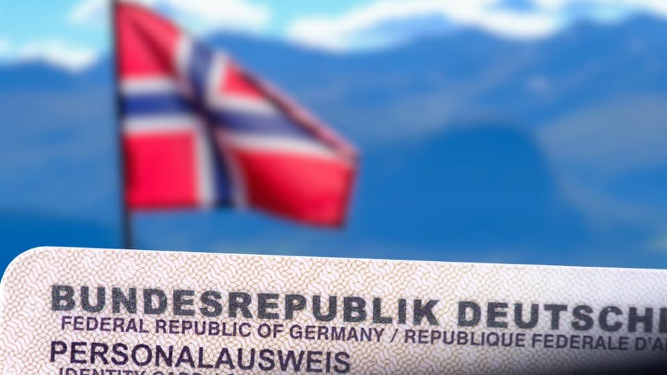 German ID card in foreground, blurred Norwegian flag and mountains in the background
