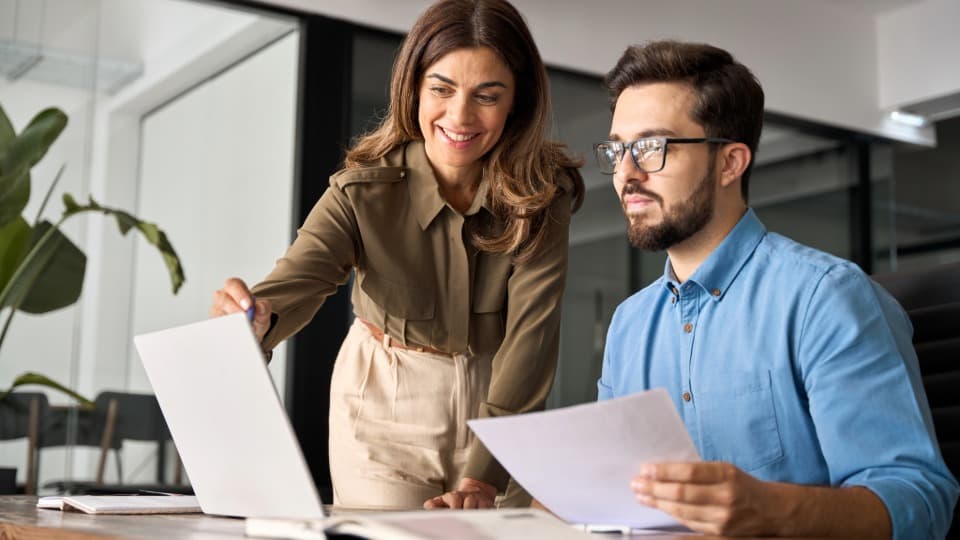 Two business partners discussing optimized workflows on a laptop in the office – professional project management and consulting for national and international facilities logistics.