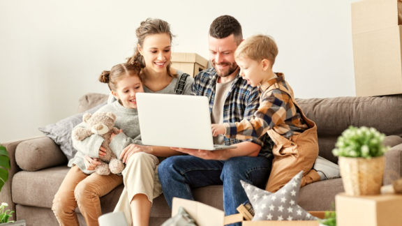 A happy family using a laptop together to calculate the cost of relocating to Switzerland with the digital moving cost calculator by DACHSER & KOLB.