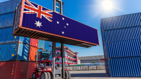 Ein Containerstapler verlädt einen Übersee-Container mit australischer Flagge für den Container-Umzug nach Australien mit DACHSER & KOLB.
