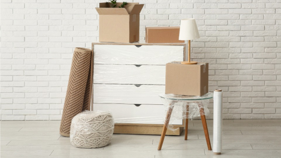 Eine folierte Kommode, ein Teppich und gepackte Umzugskartons vor einer weißen Wand als typische Beispiele für den Kleintransport mit DACHSER & KOLB.