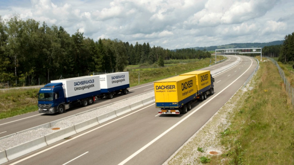 Ein Lkw von DACHSER & KOLB Umzugslogistik und ein Lkw von DACHSER Intelligent Logistics nebeneinander auf einer Straße während des Transports in Europa.