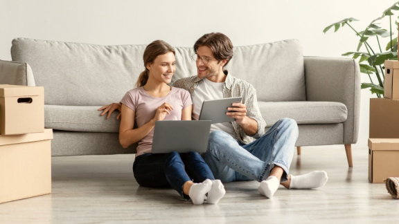 A happy couple using a laptop and tablet to calculate relocation costs for Australia with the online moving calculator from DACHSER & KOLB.