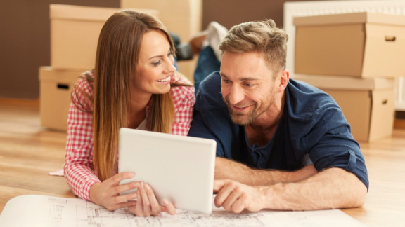 A happy couple using a tablet to calculate relocation costs for the UAE with the online moving calculator from DACHSER & KOLB.