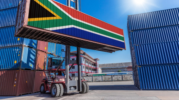 A container handler lifting a shipping container with the national flag of South Africa for customs clearance with DACHSER & KOLB.