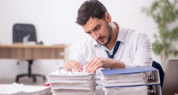 Beamter prüft Unterlagen zum Unmelden nach dem Umzug an einem überfüllten Schreibtisch im Amt.