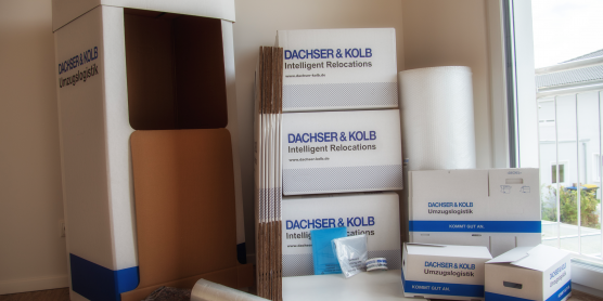 Kartons, Polsterfolie und Umzugszubehör in einer hellen Wohnungsecke bereitgestellt.