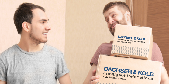 Zwei Männer tragen lachend Umzugskartons – Beispiel dafür, wie man Umzugskartons richtig packen und transportieren kann.