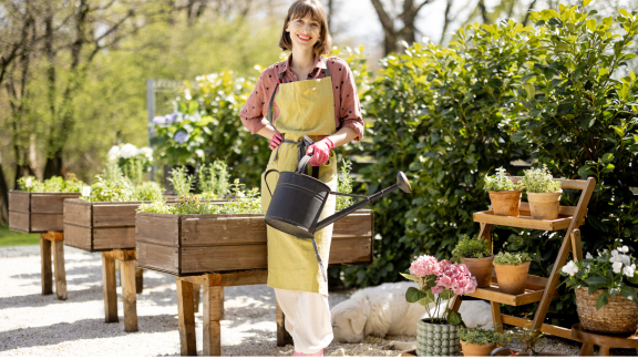 Frau gießt Hochbeet im Garten – Garten- und Landschaftsgestaltung nach dem Umzug.