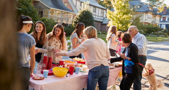Nachbarschaftsfest auf der Straße mit Tisch voller Essen und freundlichen Nachbarn. Nachbarschaft kennenlernen nach dem Umzug.
