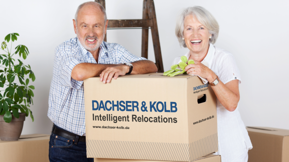 Lächelndes Seniorenpaar mit Umzugskarton – stressfreier Seniorenumzug in gehobene Wohnresidenzen mit DACHSER & KOLB