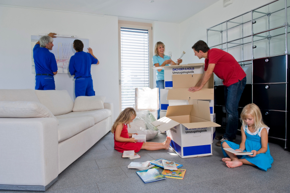 Full-Service-Umzug in Aktion: Möbelmontage, Kartons auspacken, Familie richtet sich im neuen Zuhause ein.