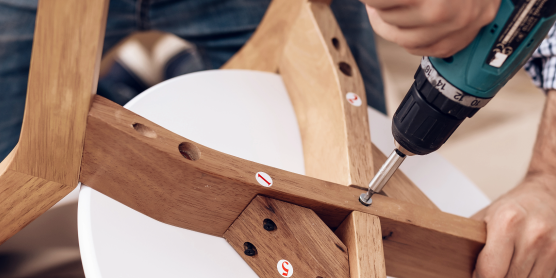 Möbelmontage leicht gemacht: Person schraubt Holzstuhl zusammen mit Akkuschrauber, Schritt-für-Schritt-Anleitung sichtbar