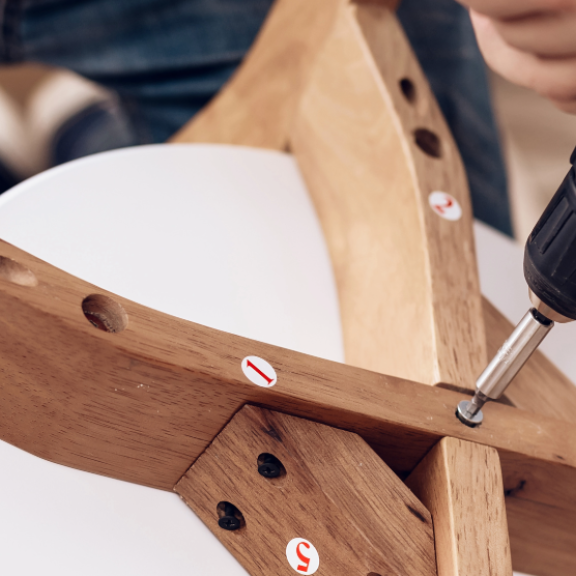 Möbelmontage leicht gemacht: Person schraubt Holzstuhl zusammen mit Akkuschrauber, Schritt-für-Schritt-Anleitung sichtbar