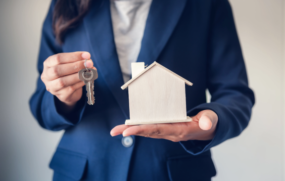 Person übergibt Schlüssel und Modellhaus – symbolische Darstellung einer Wohnungsübergabe