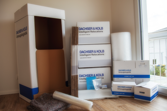 Kartons, Polsterfolie und Umzugszubehör in einer hellen Wohnungsecke bereitgestellt.