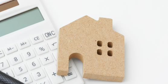 Taschenrechner, Stift und Holzhaus – Symbole für finanzielle Planung und Tipps zur Berechnung von Umzugskosten.