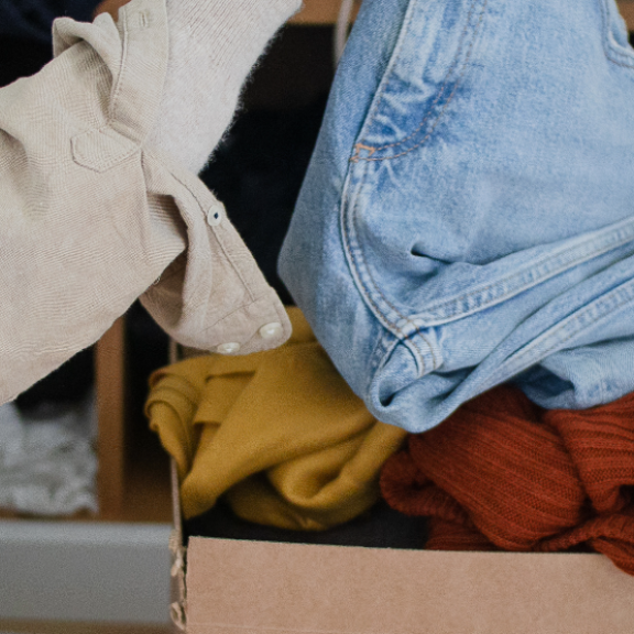 Person entsorgt Kleidung in einem Karton