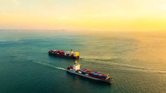 Beladenes Containerschiff einer Reederei am Kai im großen Hafen mit Kranen bei Sonnenuntergang.