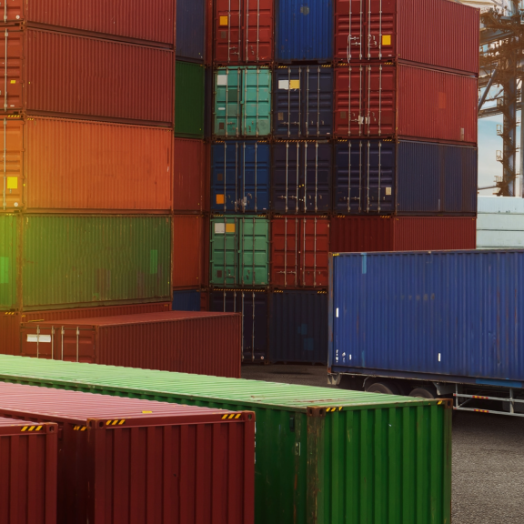 Container im Hafen für internationale Umzüge per LCL, LKW bereit zur Beladung, Schiff im Hintergrund.