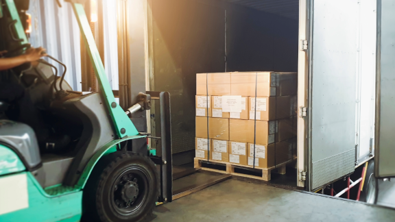 Gabelstapler belädt einen LKW mit Kartons auf Paletten. Keine Holzkisten (Crates) sichtbar. Logistik und Transport.