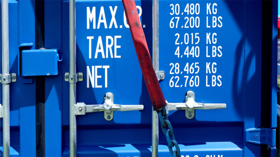 Nahaufnahme der Beschriftung eines blauen Frachtcontainers mit Gewichtsangaben, die die Relevanz des Volumengewichts im globalen Versand verdeutlichen.